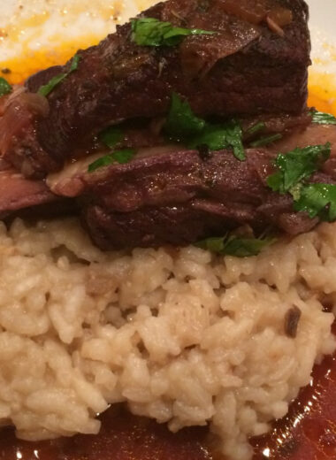 A bowl with risotto and wine braised beef ribs on it.