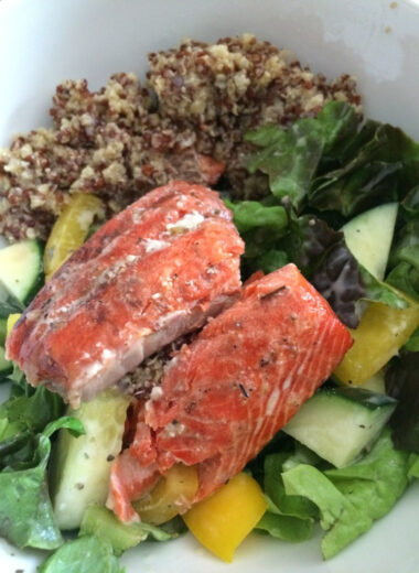 A bowl full of quinoa, vegetables and cedar plank salmon.