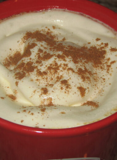 A red cup holding coffee with whipped cream and cinnamon on top.