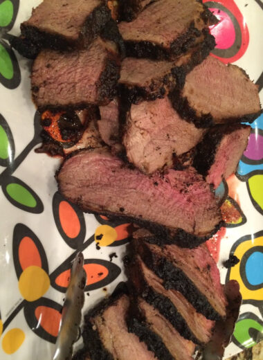 A colorful platter with coffee rubbed tri tip sliced on it.