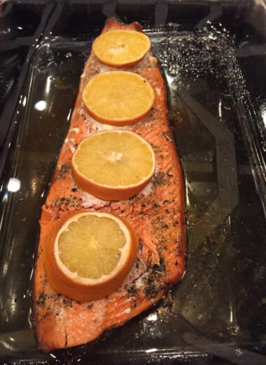 A pan with a large piece of salmon toped with oranges in it.