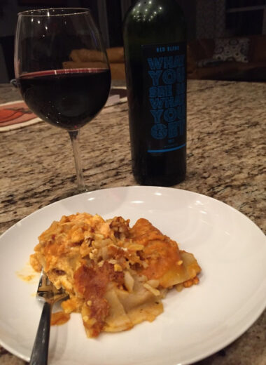A plate with gluten free pumpkin lasagna on it with a wine glass full of wine beside it.