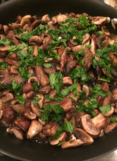 A pan full of sautéed mushrooms with fresh herbs on top.