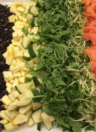 A platter with rows of smoked salmon, chopped arugula and other vegetables on it to make a delicious salad.