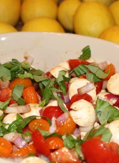 A bowl full of chopped tomato, mozzarella, fresh basil and balsamic vinegar for a caprese salad.