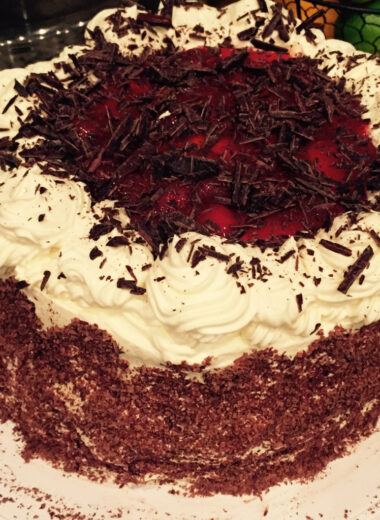 A picture of a gluten free black forrest cake with whipped cream, cherries and chocolate shavings.