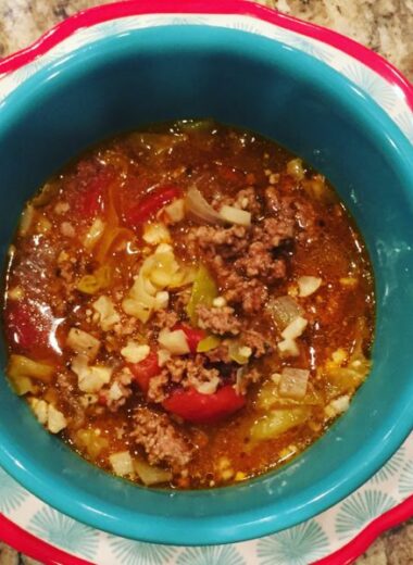 A pretty blue bowl on a red and bowl plate with cabbage roll soup inside of it.