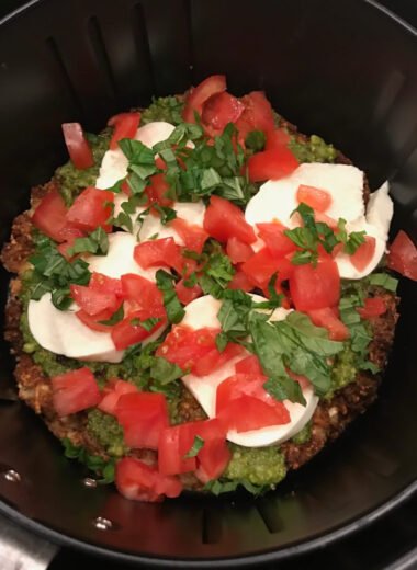 An air fryer basket filled with a crispy cauliflower crust topped with Caprese salad ingredients.