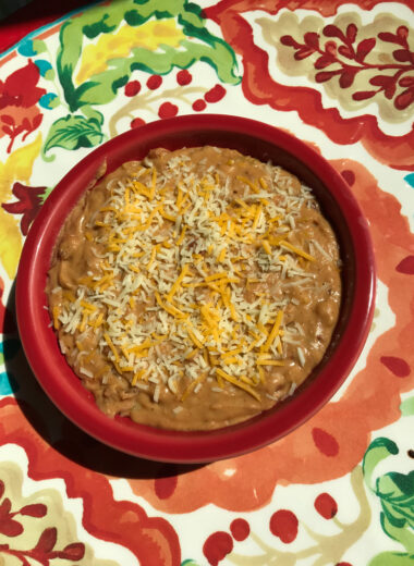 A colorful platter with red bowl on it full of refried beans.