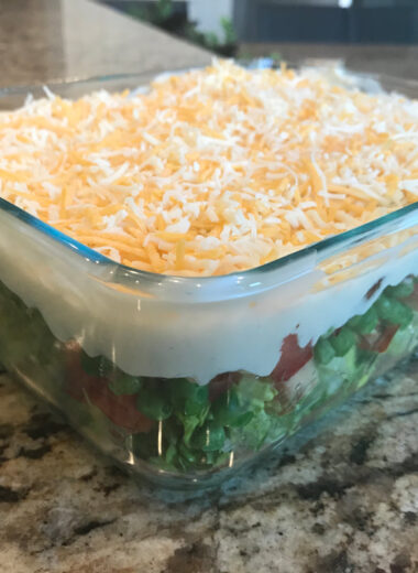 A casserole dish on the counter filled with vegetables and dressing to make a seven layer salad.