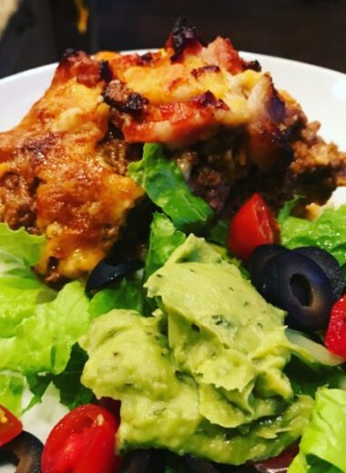 A white plate with green salad and tomatoes on it and a slice of taco meat pie.