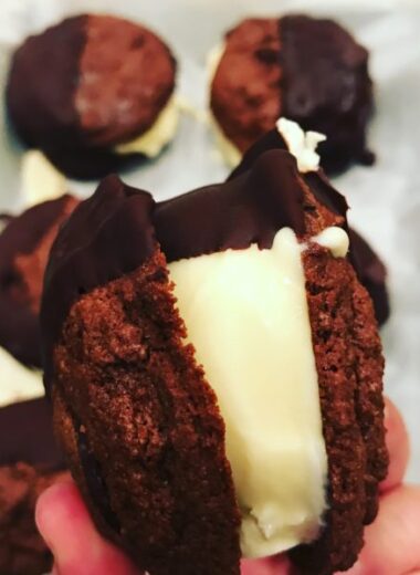 Two chocolate cookies with ice cream in the middle dipped in dark chocolate.