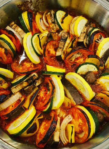 A pan full of different colored vegetables such as zucchini, eggplant, squash, tomatoes and tomato sauce.