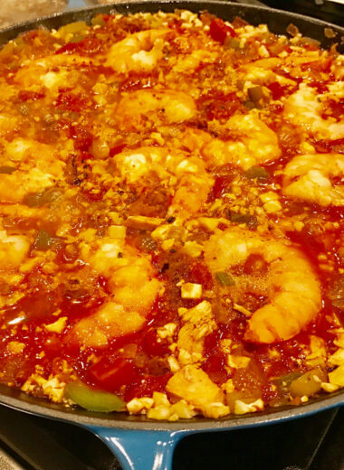 A blue pan filled with shrimp, veggies and sauce to make a delicious paella