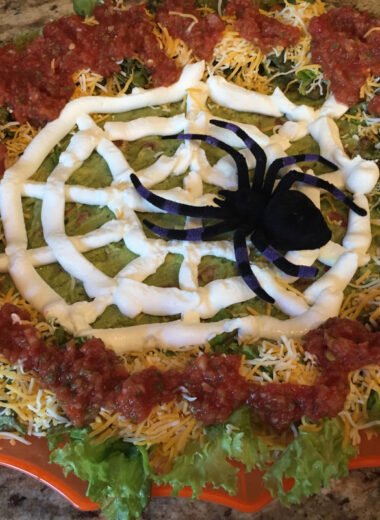 A party tray with lettuce cheese beans and a spider decorated to look like a spider sitting on a web.