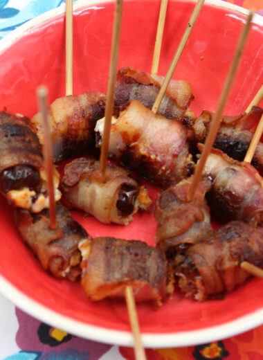 A colorful mat with a red bowl filled with dates wrapped in bacon and stuffed with cheese.