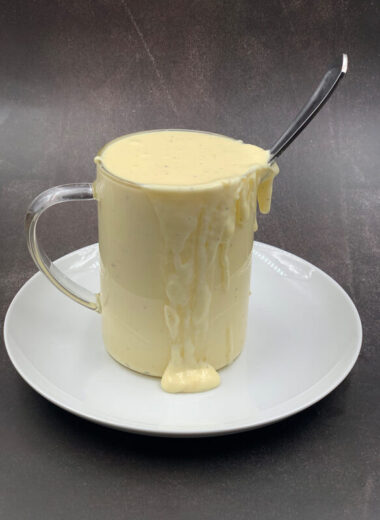 A glass jar sitting on top of a white plate with creamy sauce dripping out of it with a spoon inside the jar.