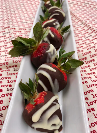 A red and white background with a white rectangular dish on it filled with dark and white chocolate dipped strawberries in it.