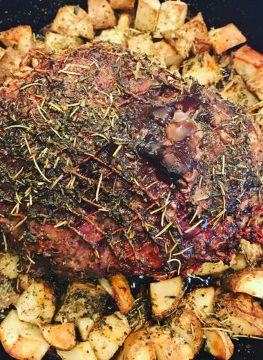 A cast iron pan with a roast in the middle surrounded by cubed potatoes.
