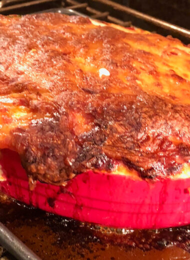 A red baking dish full of food with tomato sauce and melted cheese over the top.