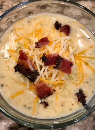 A bowl full of soup with broccoli, cheese and bacon on top.
