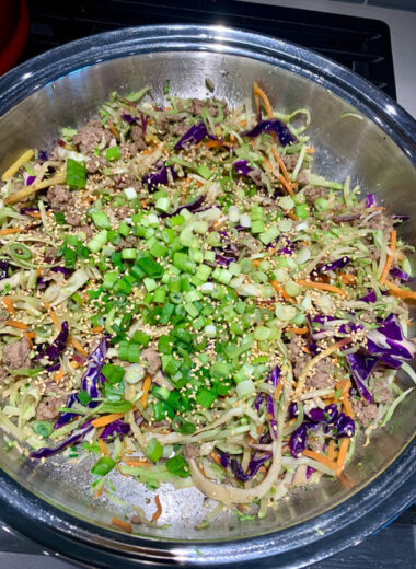 A stainless steel pan with multi colored cabbage, carrots, green onions and other veggies in it.