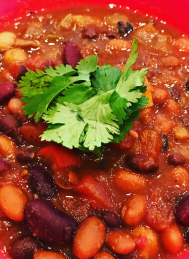 A red bowl with sauce and beans in it topped with fresh cilantro.