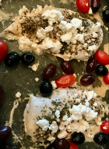 A pyrex baking dish filled with chicken breasts, tomatoes, olives, feta and other seasonings.