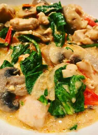 A white bowl full of creamy broth, chicken and vegetables.