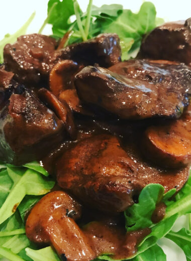 A white plate with arugula on it topped with steak bites and mushrooms in a sauce.