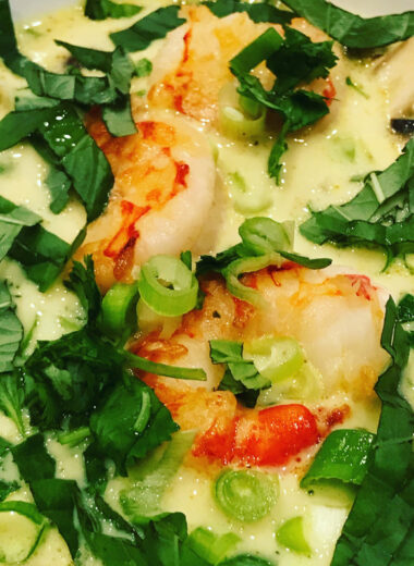 A bowl full of creamy soup with herbs and cooked shrimp and chicken in it.