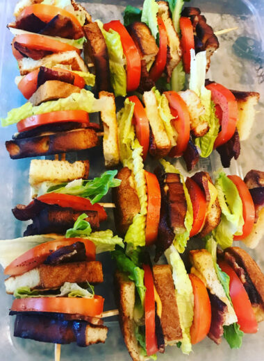 A platter with Bacon Lettuce and Tomato layered sandwiches on it that have a skewer stuck through them holding it together.