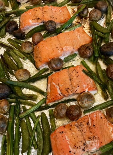 A foil lined pan with cooked salmon, mini potatoes, green beans and snap peas on it.