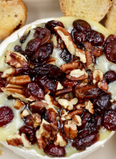 A baking dish with melted cheese, cranberry and pecans with toasted bread around it.