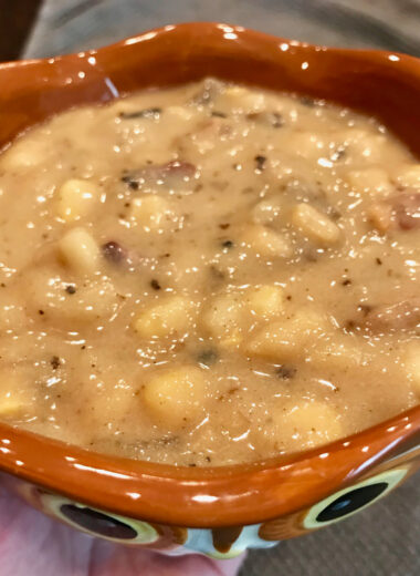 A brown bowl that looks like an owl with creamy soup inside of it.