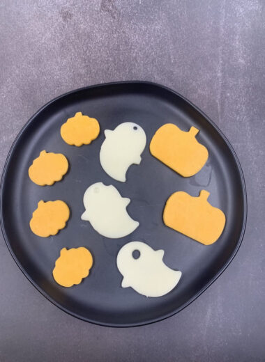 A black plate with orange pumpkin cheese cut outs, and white ghost cut out of cheese.