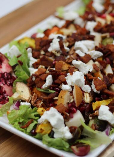 A white platter with lettuce, pomegranate, pears, goat cheese, nuts and other veggies on it for a delicious salad.