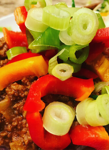 A plate with a sweet potato with chili inside of it and green onions, and peppers on top of it.