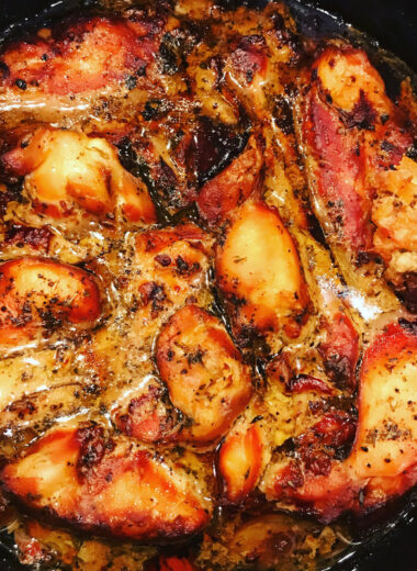 A black pot with roasted chicken in it covered in a sauce.