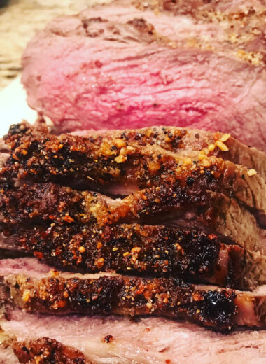 A Roast of meat on a platter that is sliced and cooked perfectly medium rare.