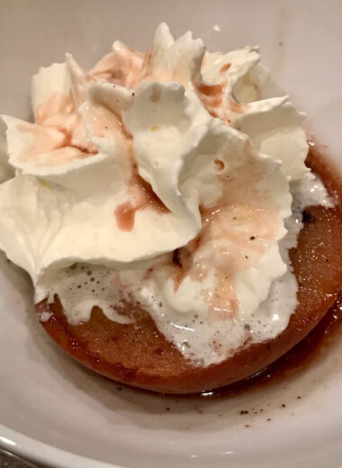 A white bowl with a wine colored pear half in it covered in whipped cream.