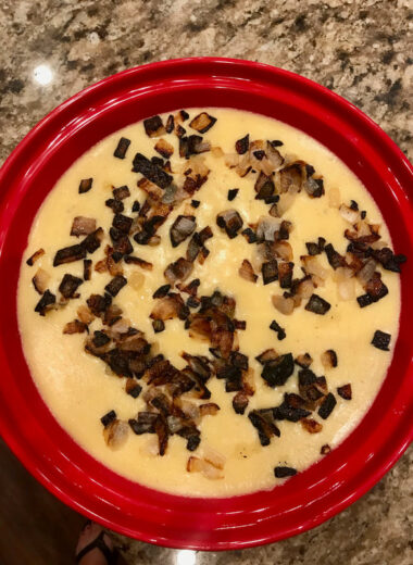 A red bowl holding soft polenta topped with crispy fried onions.