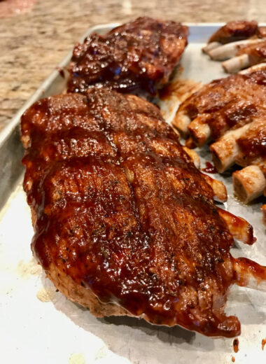 A sheet pan with racks of ribs with BBQ sauce on them.