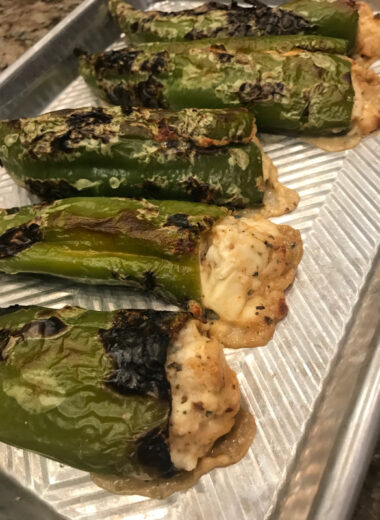A metal pan with jalapeno peppers with cheese melting out of them.