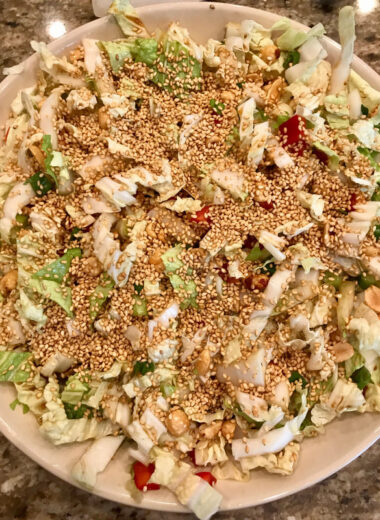 A bowl with napa cabbage, peppers, sesame seeds, onions and other vegetables in it.