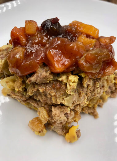 A square of egg bake like food topped with delicious fruit chutney on a white plate.