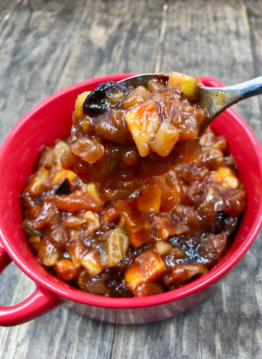 A red cup with pieces of fruit in a sauce in it and a spoon scooping some of it out.