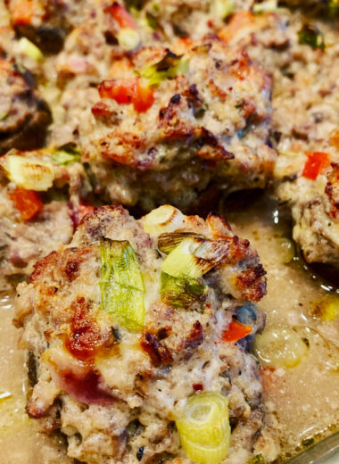 A pan with mushrooms stuffed with melted cheese, vegetables and sausage in them.