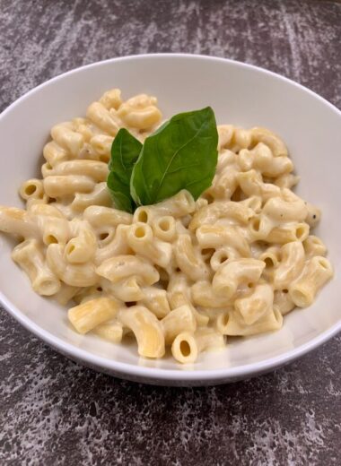 A white bowl full of creamy macaroni topped with basil.