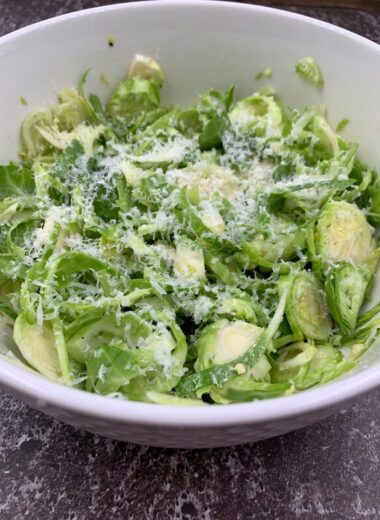 A white bowl with shredded Brussels Sprouts and cheese in it.